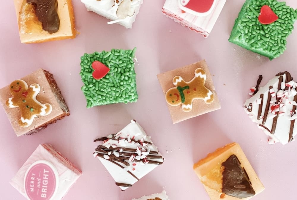 Various colorful, square-shaped sweets are pictured on a pink table.