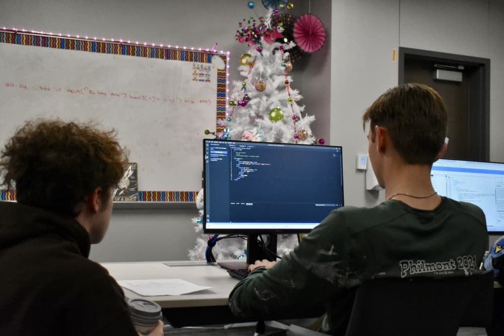 two students look at a computer while working on coding