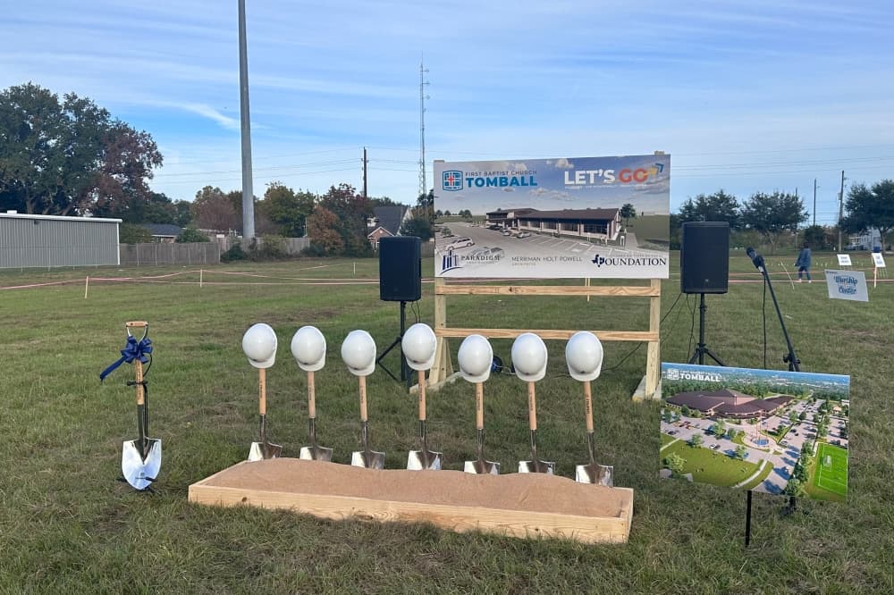 Shovels in dirt in a row with hard hats hanging off of them