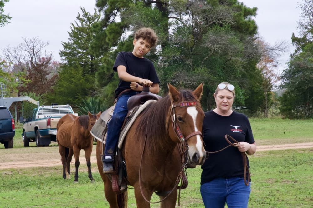 A volunteer from Cherokee Outlaw Ranch helps guide a child around the ranch on horseback.