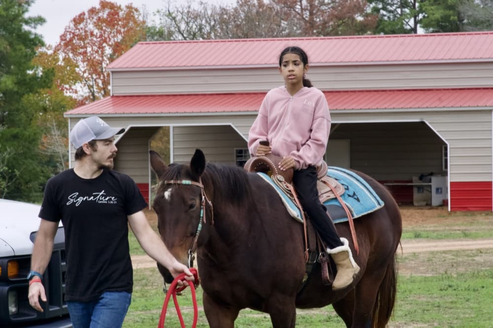 A volunteer from Cherokee Outlaw Ranch helps guide a child around the ranch on horseback.