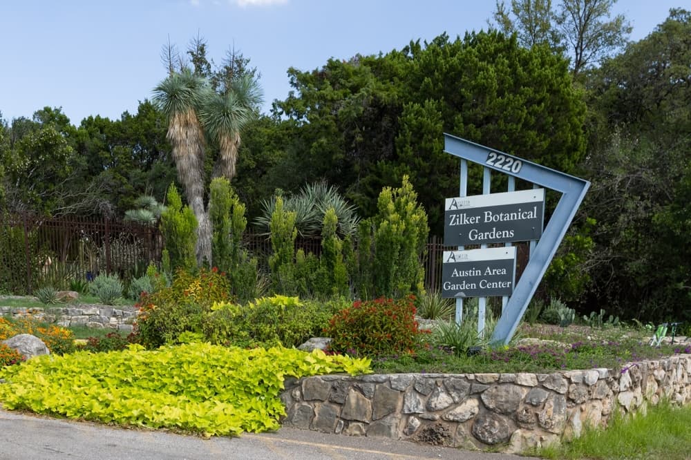 A look at a Zilker sign in the gardens with trees in the background.