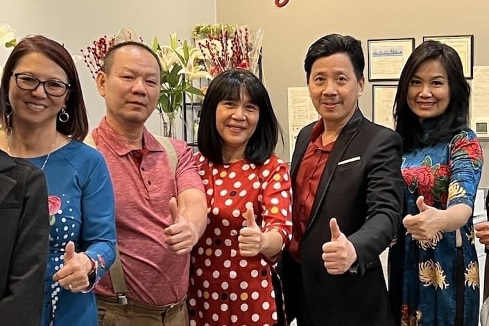 The five owners of Pho Phong Luu, stand inside the restaurant holding their thumbs up.