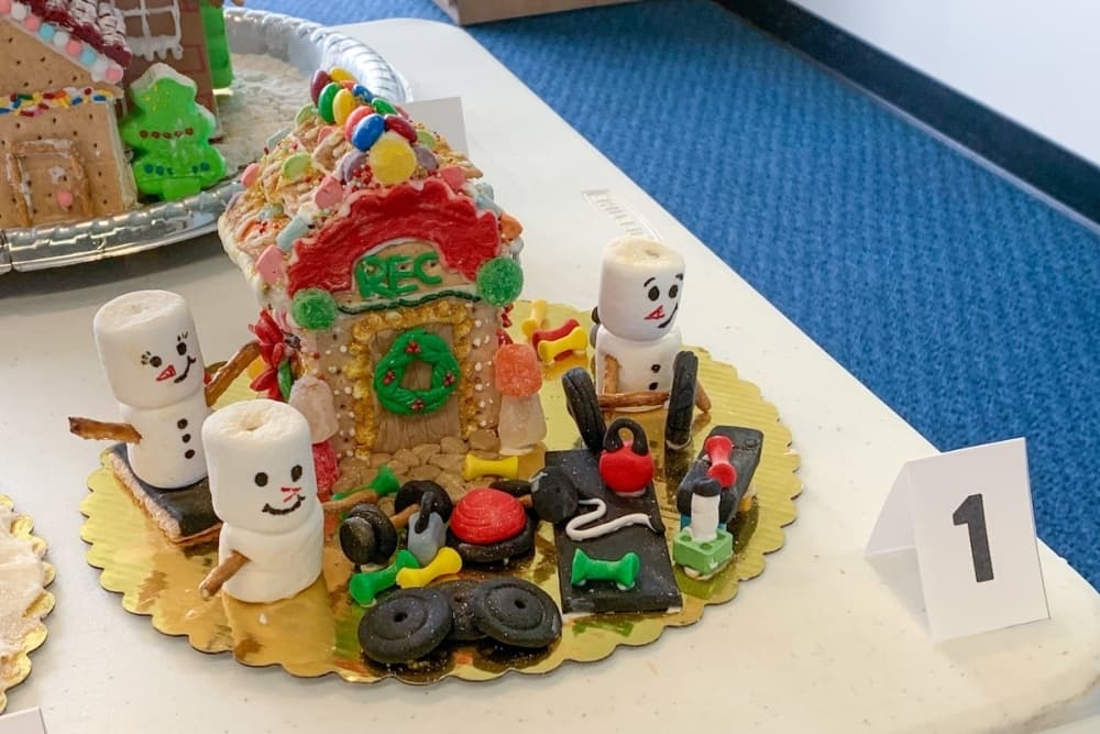 A decorated graham cracker house with marshmallow snowmen and other candies is shown.