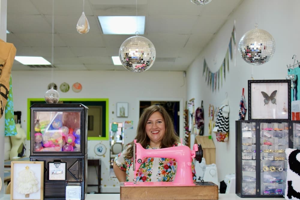 Owner in front of pink sewing machine and disco balls floating 