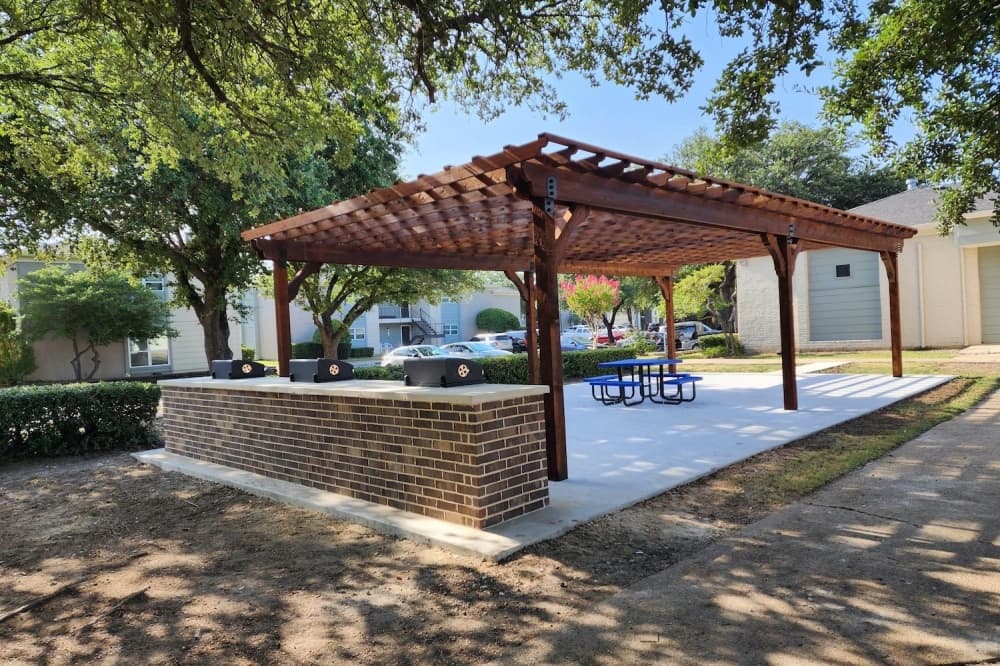 An outdoor area with grills, a picnic table and a gazebo structure overhead. 
