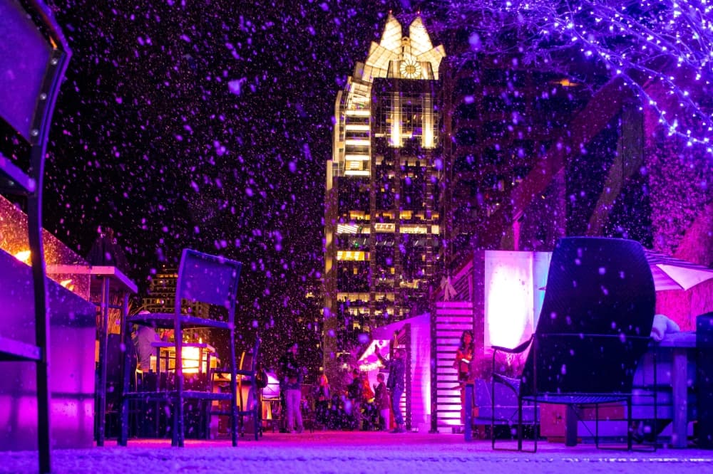 The rooftop bar is lit in blue and purple lights while it snows with the snow machine.