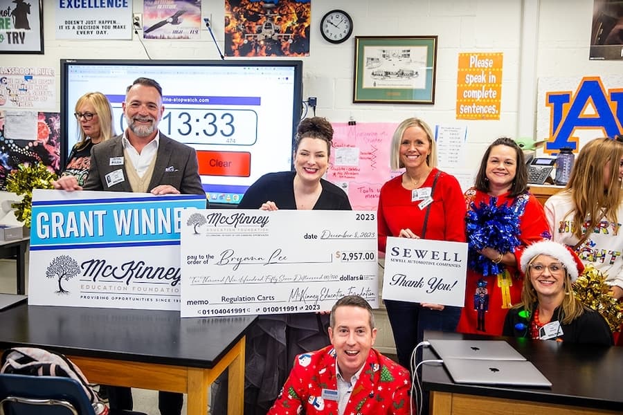 a group of people pose in a classroom with a large cheque