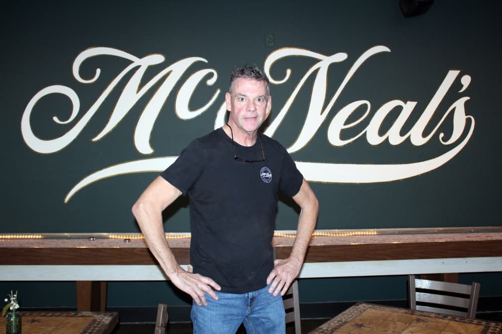 Tom McGill, owner of McNeal's Tavern standing in front of business sign. 