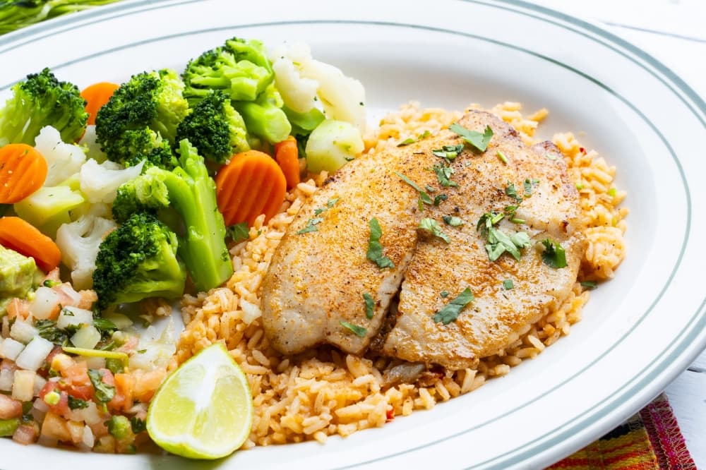 Tilapia served on bed of rice with broccoli and carrots 