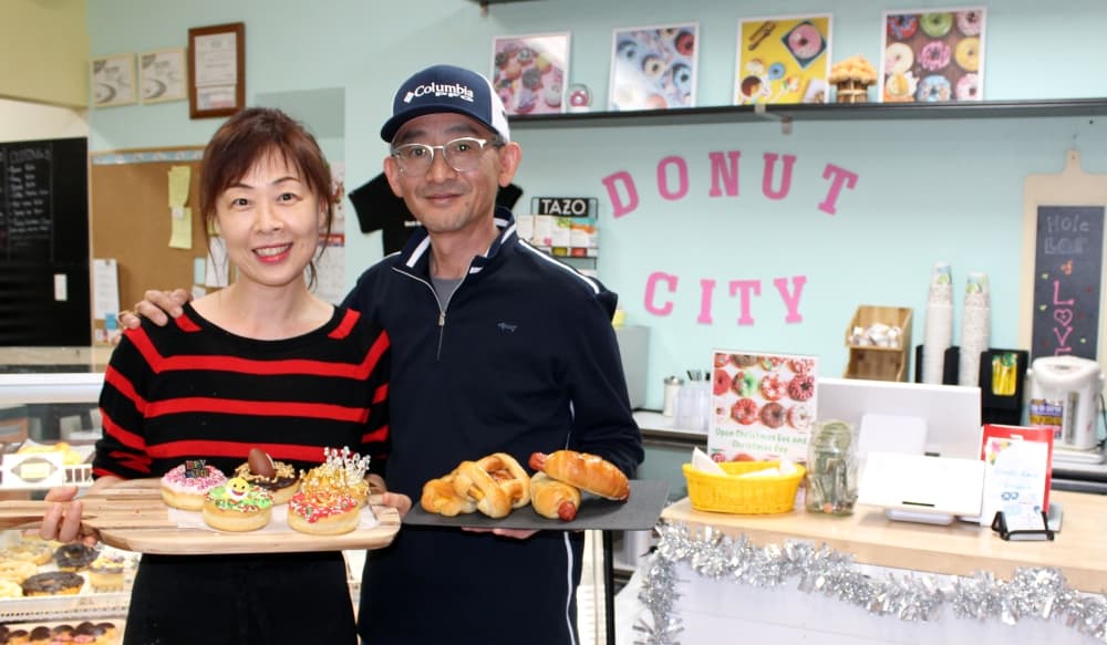 Owners of Donut City holding trays of donuts, kolaches