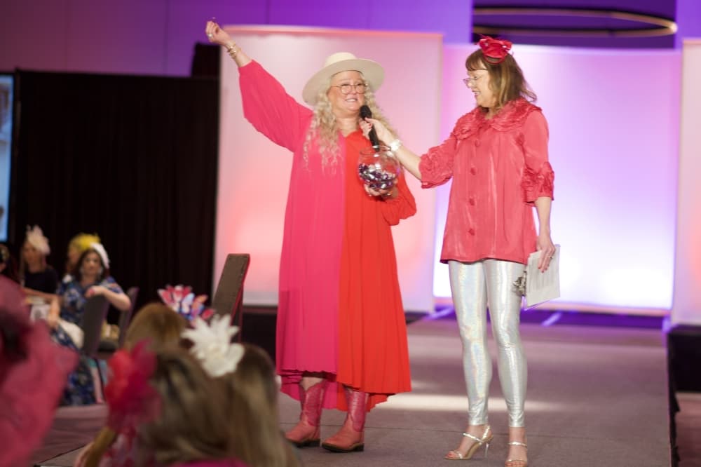 Two women stand on the stage while interacting with the audience.