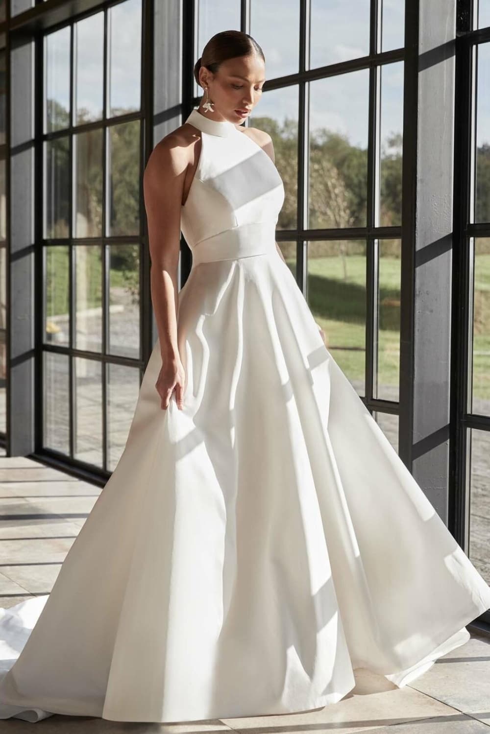 Woman wearing bridal gown near floor to ceiling windows.