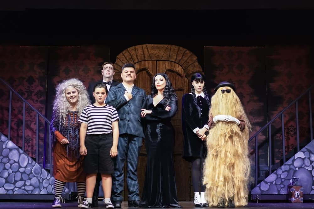 Actors dressed as the Addams Family on a set stage.