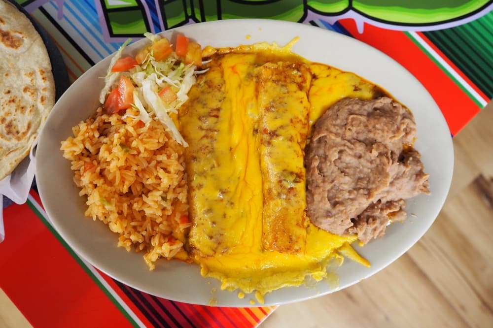 cheese enchiladas, rice and beans on a white plate