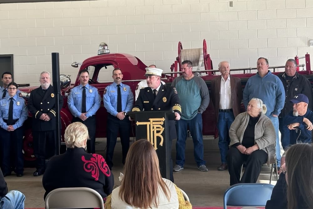 Tomball Fire Chief Joe Sykora speaks at a podium, flanked on either side by current and former Tomball firefighters