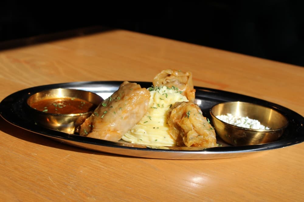 A silver plate with stuffed cabbage, sauce and mashed potatoes.