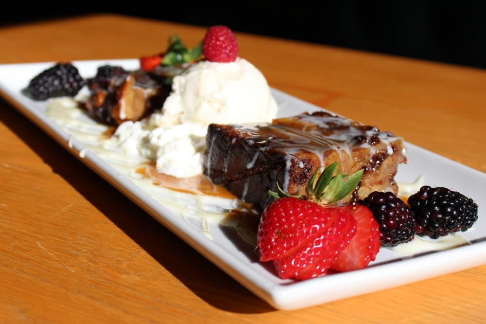 White dish with brownies drizzled with sauce, ice cream and berries.