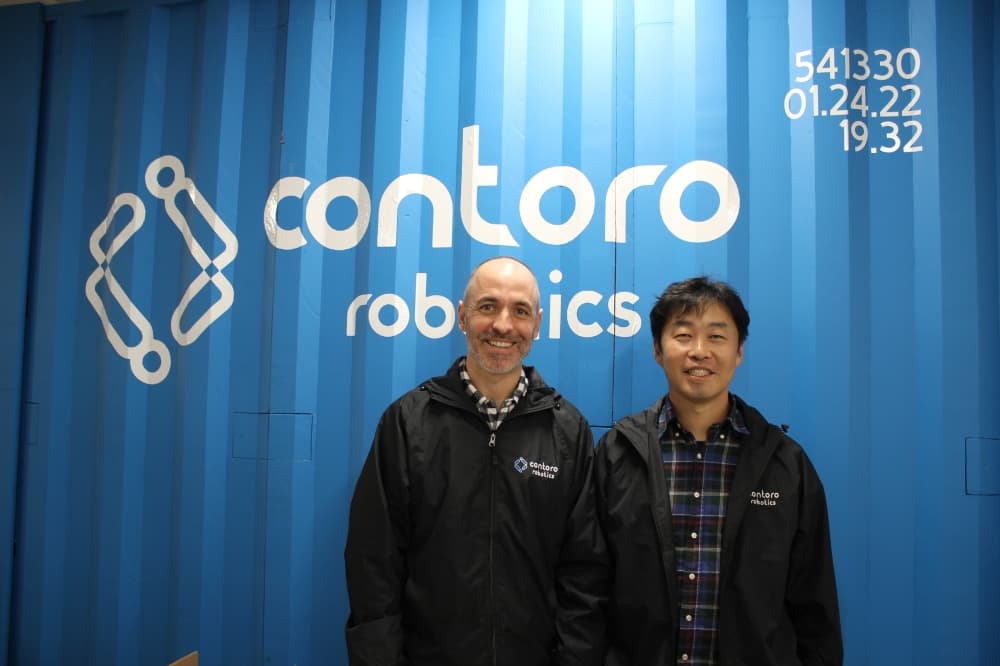 two men standing in front of shipping container