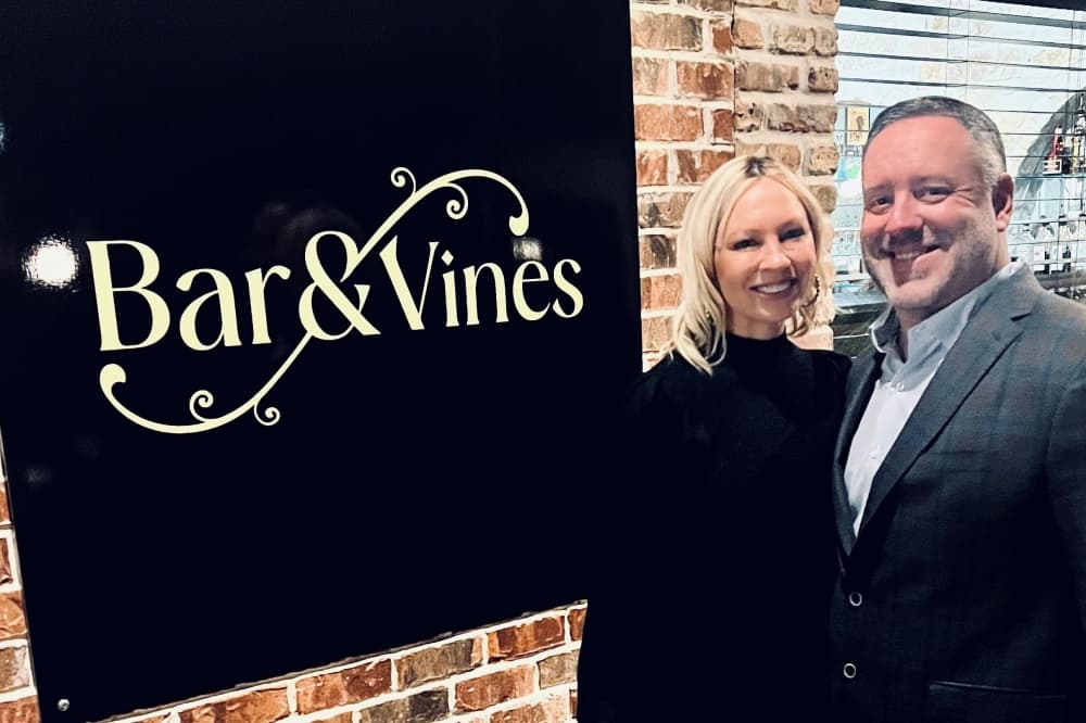Two bar owners stand in front of their bar sign