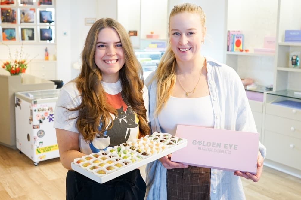The two owners pose for a photo inside the new shop while holding chocolates.