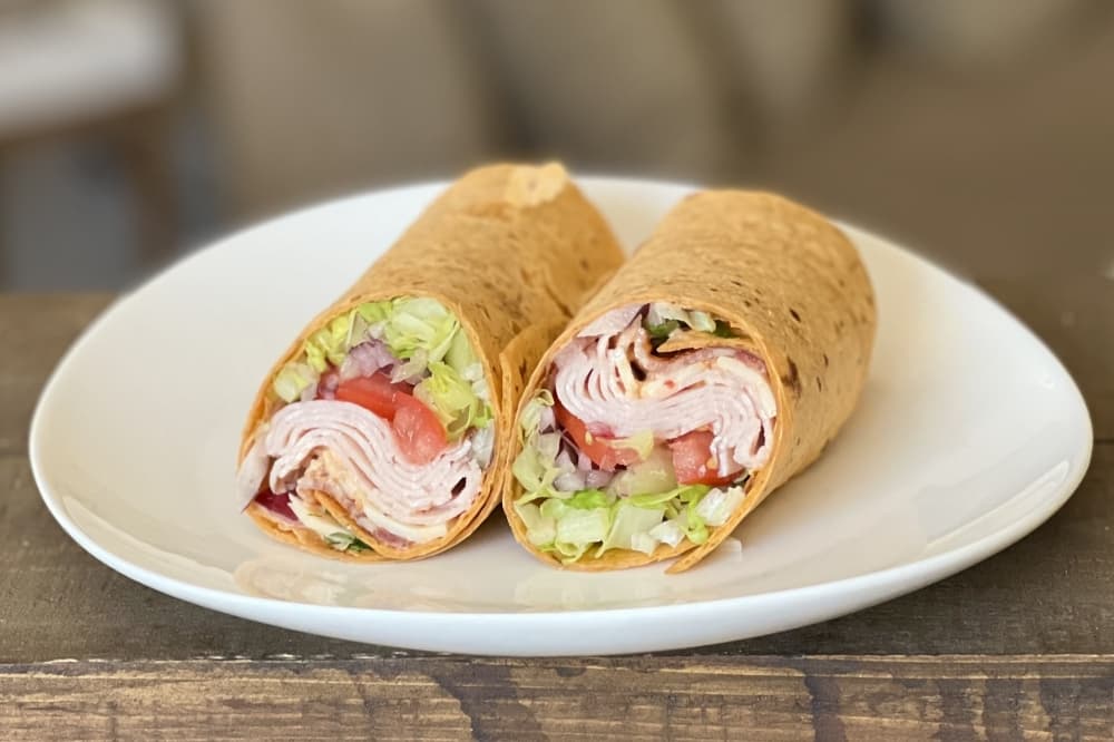 A wrap filled with meats, cheese and vegetables is shown cut in half on a white plate.