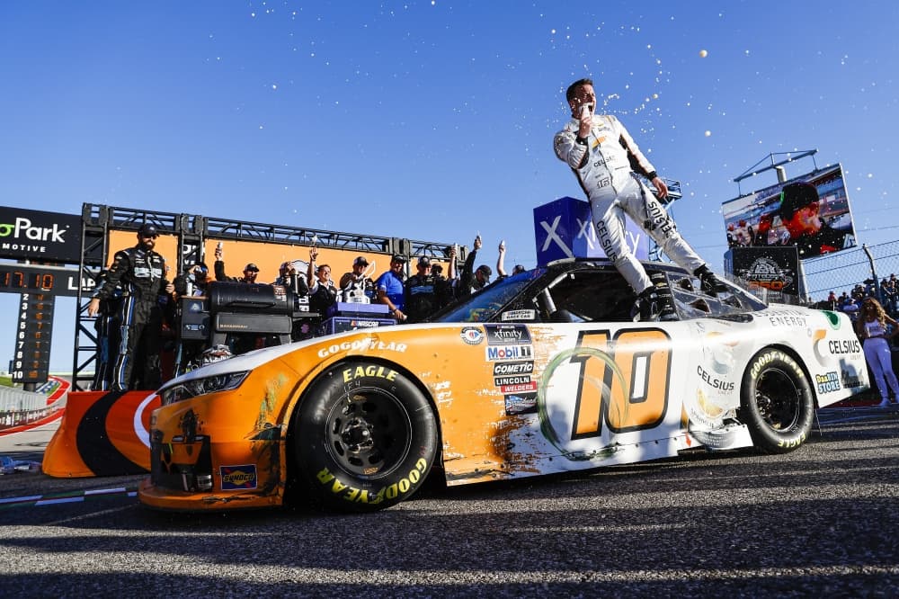A race car driver stands on top of the car celebrating.