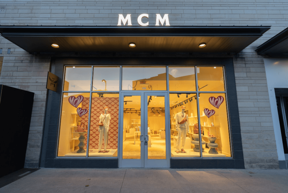 The grey storefront is shown with MCM in white letter across the top and a lighted display through the front.