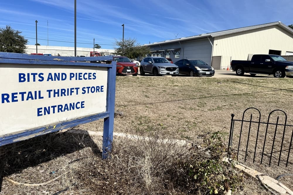A blue and white sign for Bits and Pieces Thrift Store is in the foreground with the exterior of the building in the background.