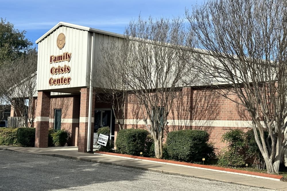 An exterior shot of the beige building with maroon letters reading "Family Crisis Center" is shown.