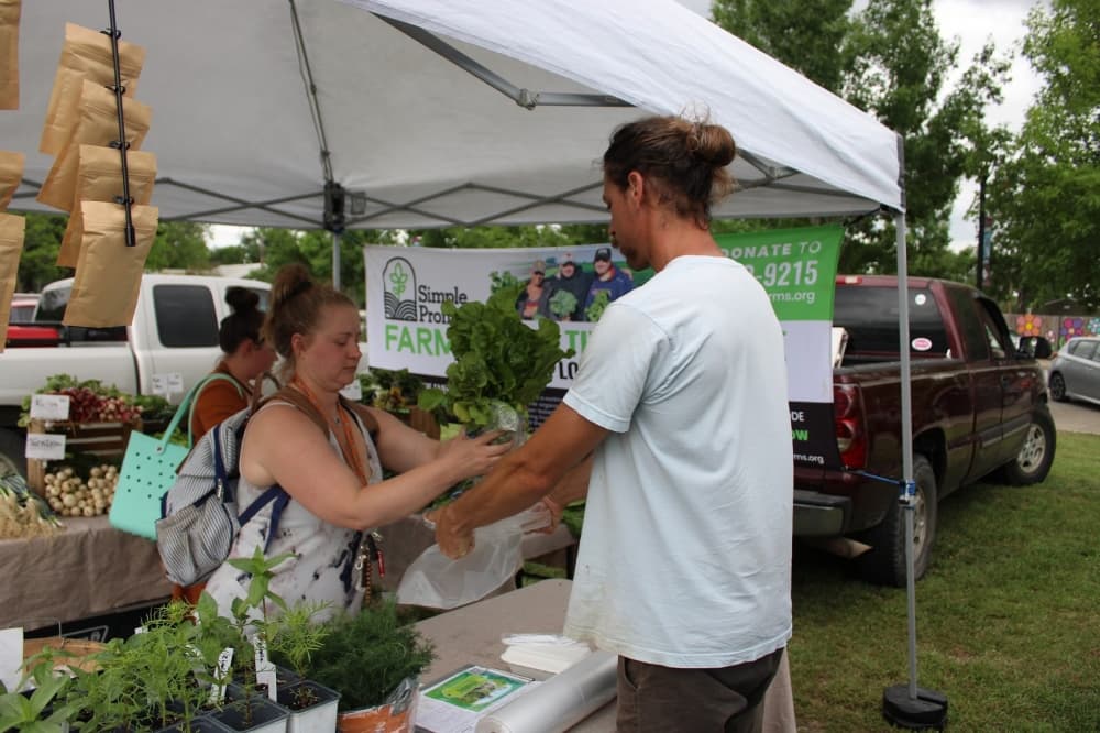A man buys fresh vegetables from a women at a farmers market stand. 