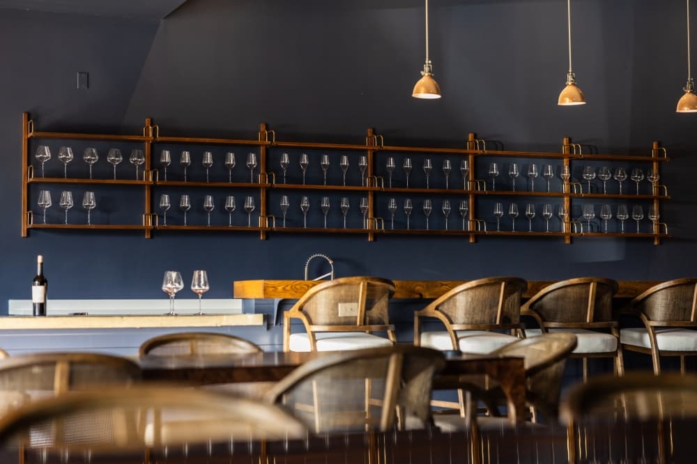 The wine tasting lounge has dark blue walls and brown chairs with hanging lights.