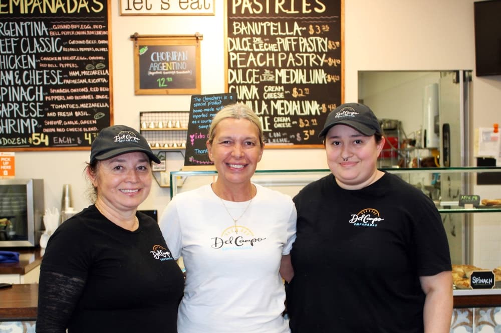 Three women standing in an empanadas store.