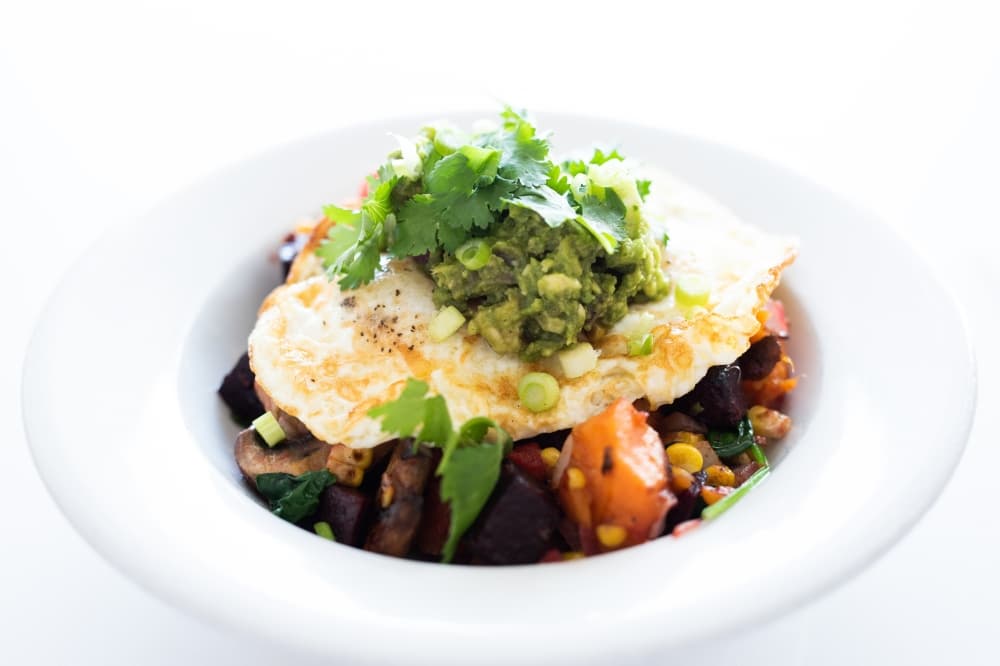 A while wide bowl holds the colorful smoked beef hash topped with green cilantro and guacamole.
