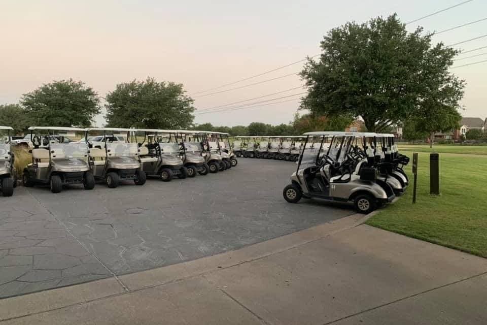 Multiple golf carts parked near a golf green. 