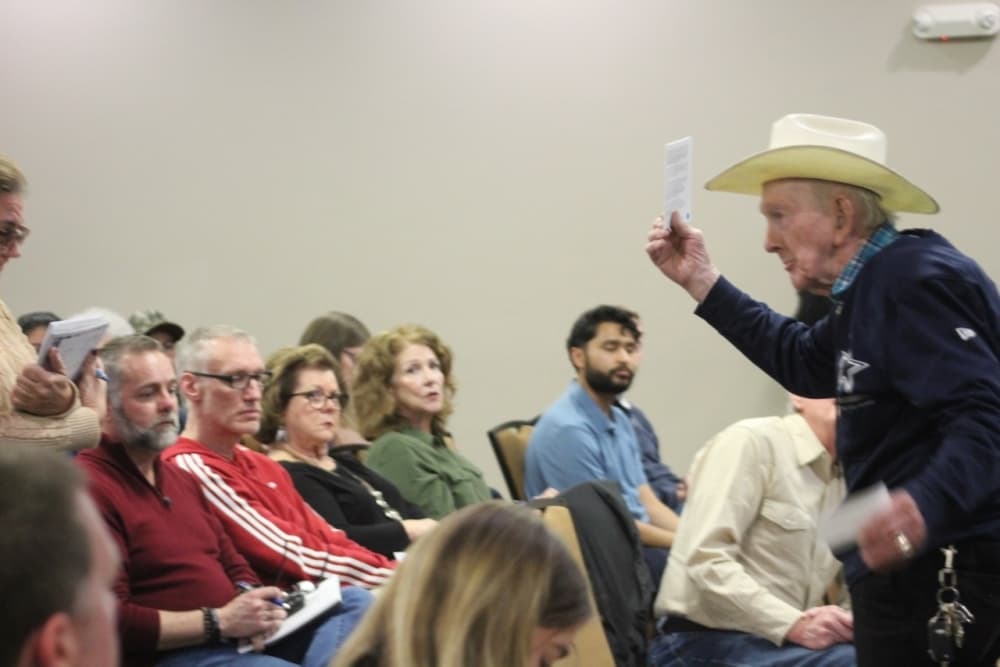 An elder man holding up a pamphlet in front of a crowd.