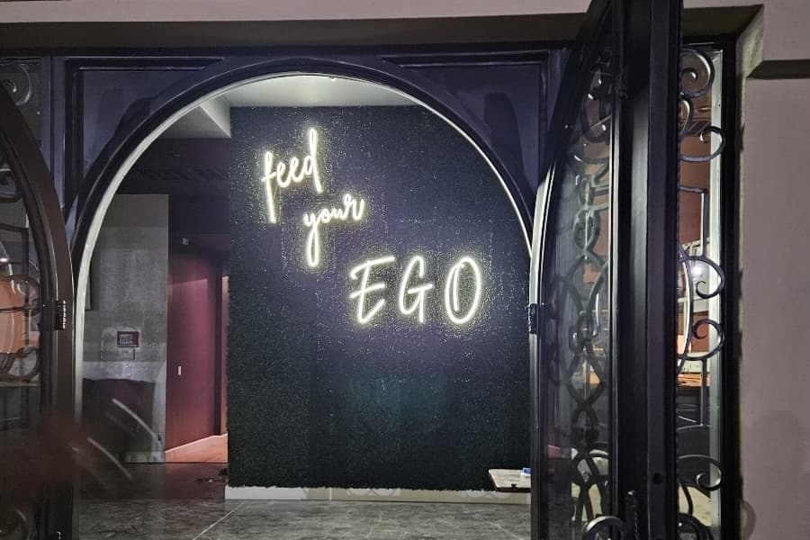 A door leading into a restaurant/bar with the neon white words "Feed your Ego" on a black wall.