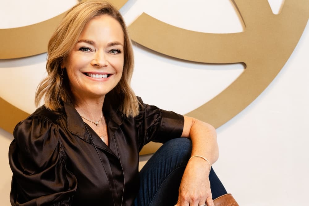 Founder Susi Transou poses and smiles for a photo, with her hand on her knee.