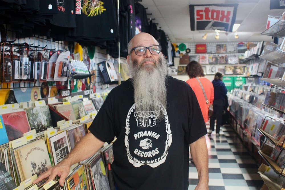 john aleman stands near a row of vinyl records in his store