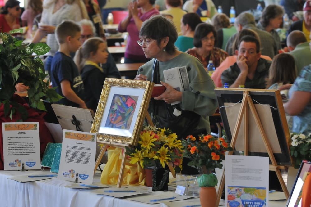 The center is filled with people in the background, as a woman in the foreground looks at the auction table.