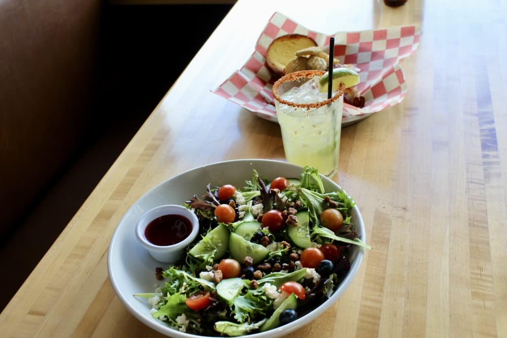 A salad with a drink and sandwich in the background