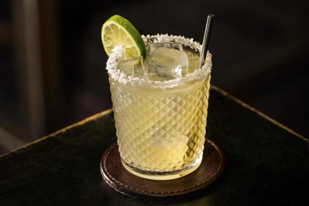 A margarita is shown in a rimmed glass, dressed with a lime slice.