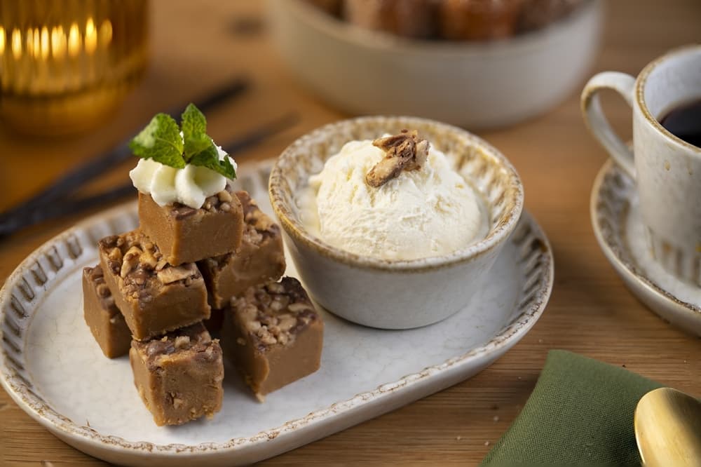 A white dish holds square brown candy on the left and a bowl of vanilla ice cream on the right.