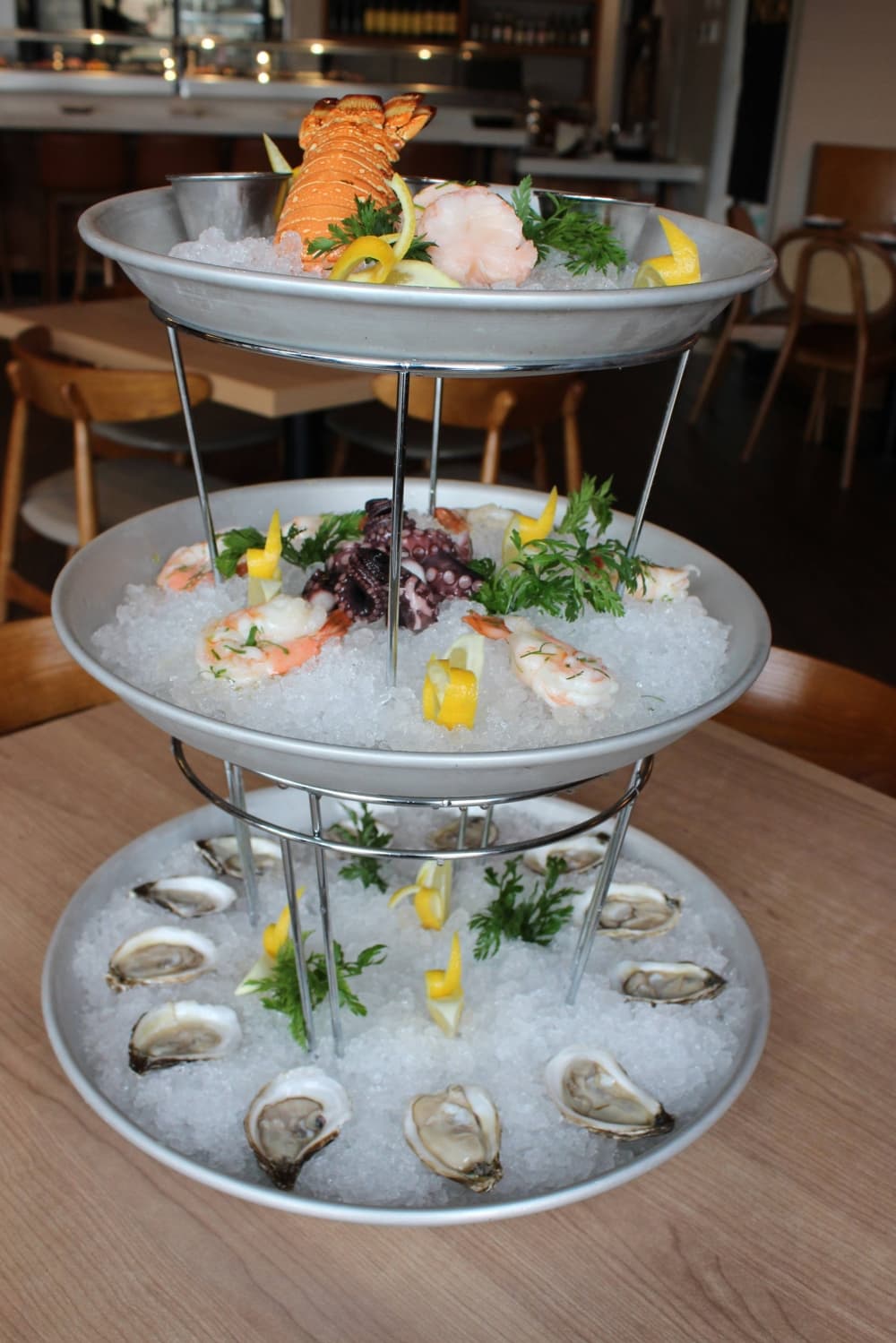 Three stacked silver trays filled with ice and a variety of seafood.