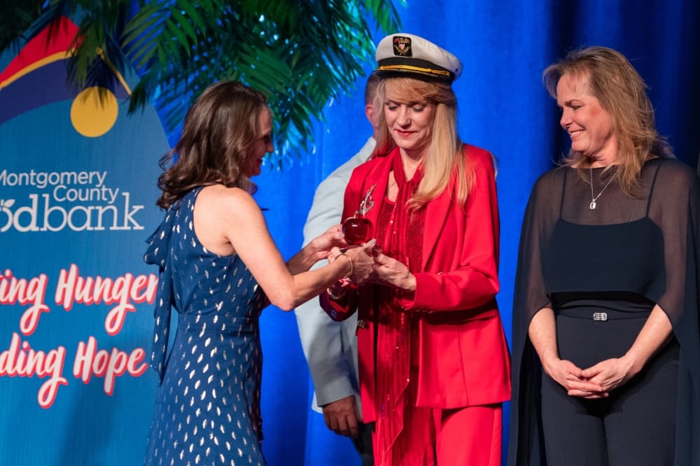 A woman hands an award to two other women standing to her right.