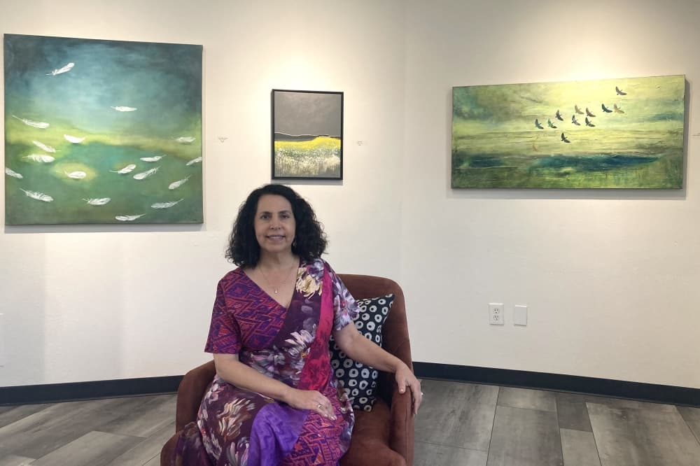 A woman sits in a room surrounded by artwork of birds
