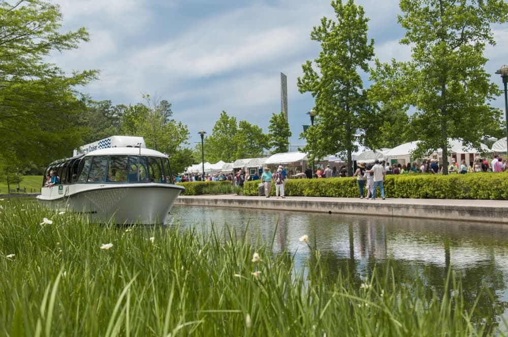 A boat travels down a stream with white tents in the background