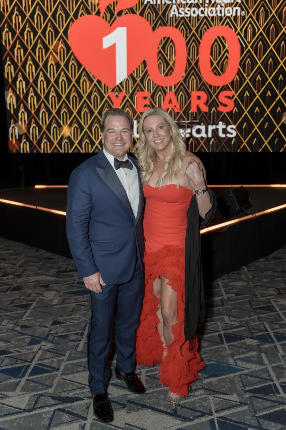 A man in a suit and a woman in a red dress post in front of a "100 years" sign.