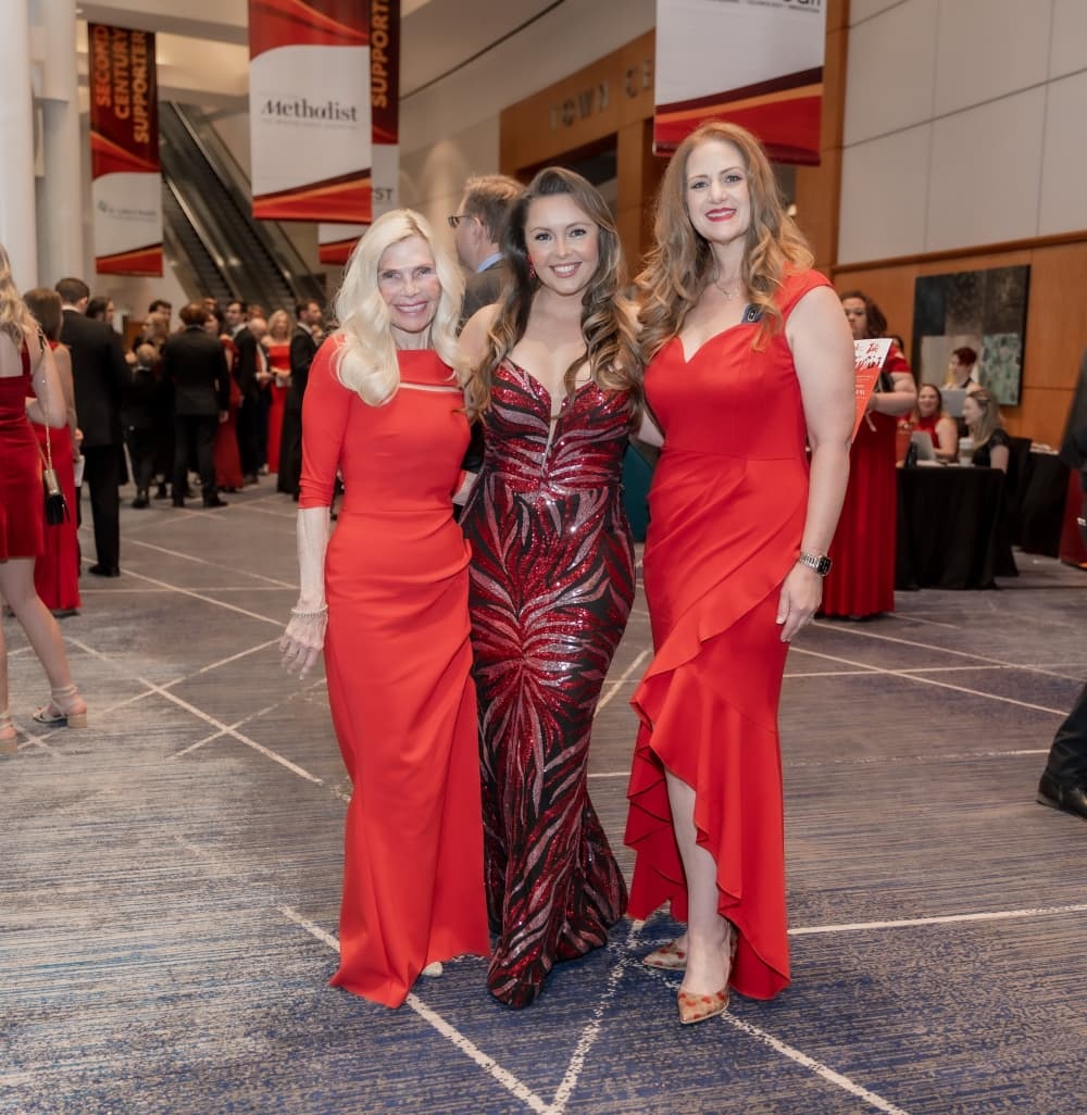 Three women in red dresses appear at a ball