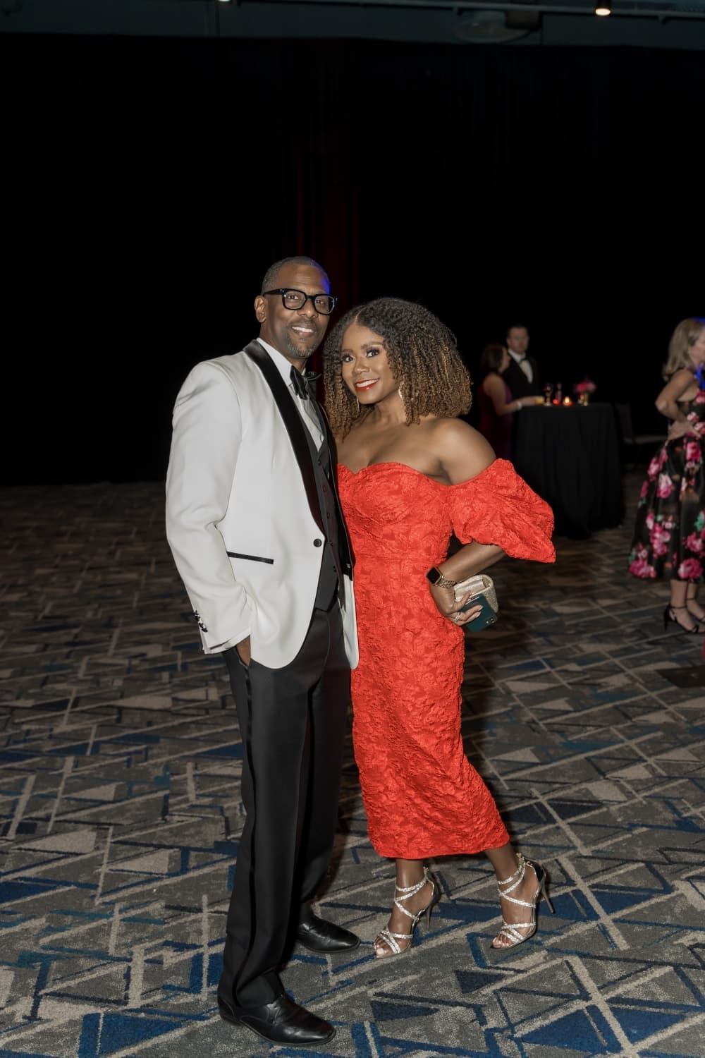 A woman in a red dress and a man in a white jacket attend the event.